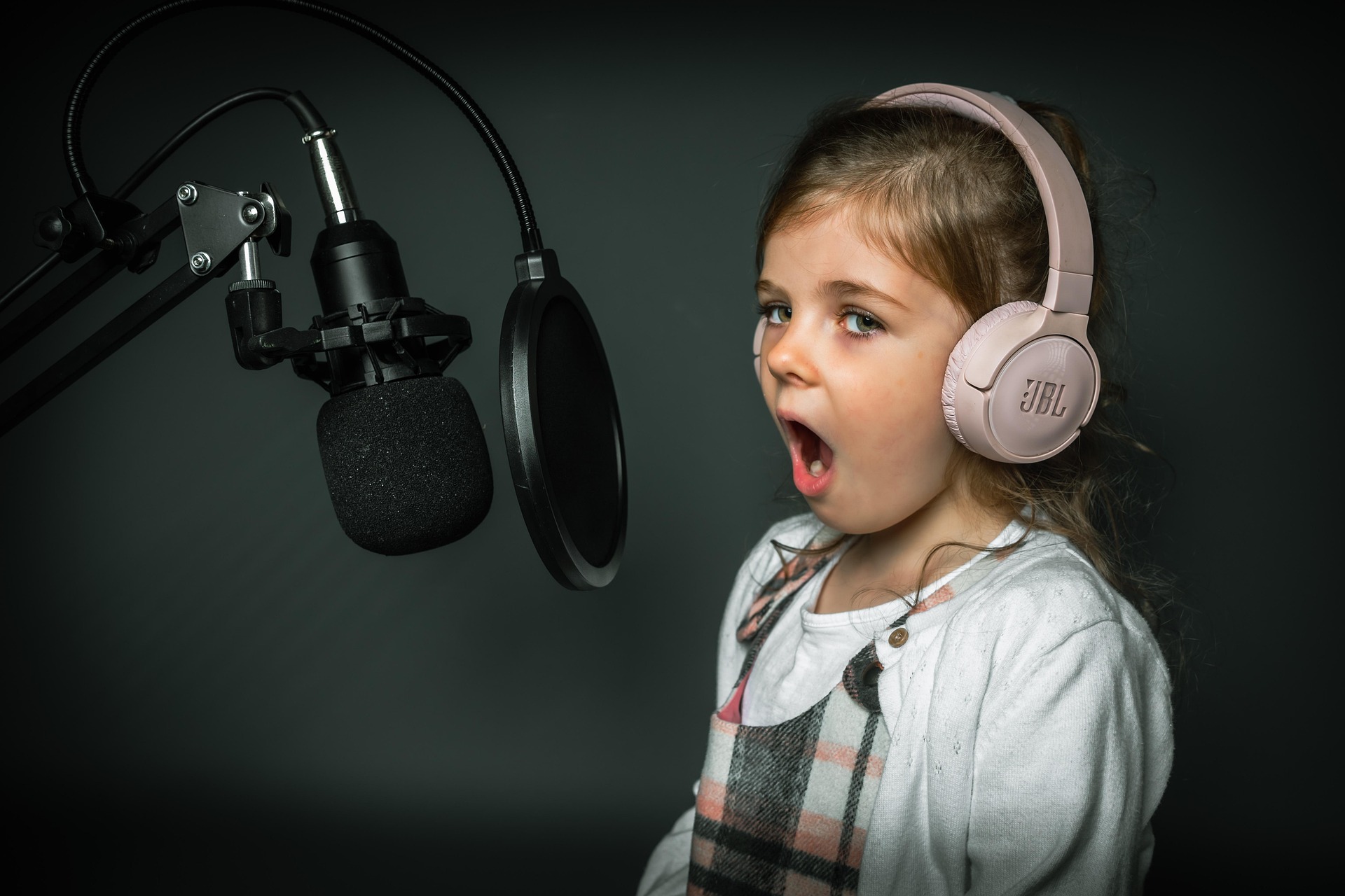 Little girl in white with pink headphones on singing into a microphone.