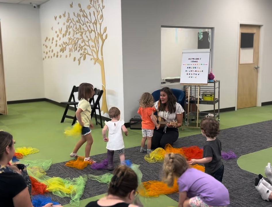 Music class with Miss Ari and a ukulele and children gathered around.