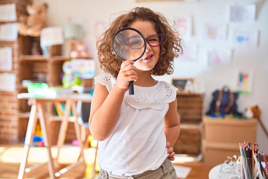 Little girl with glasses looking through a magnifying glass.