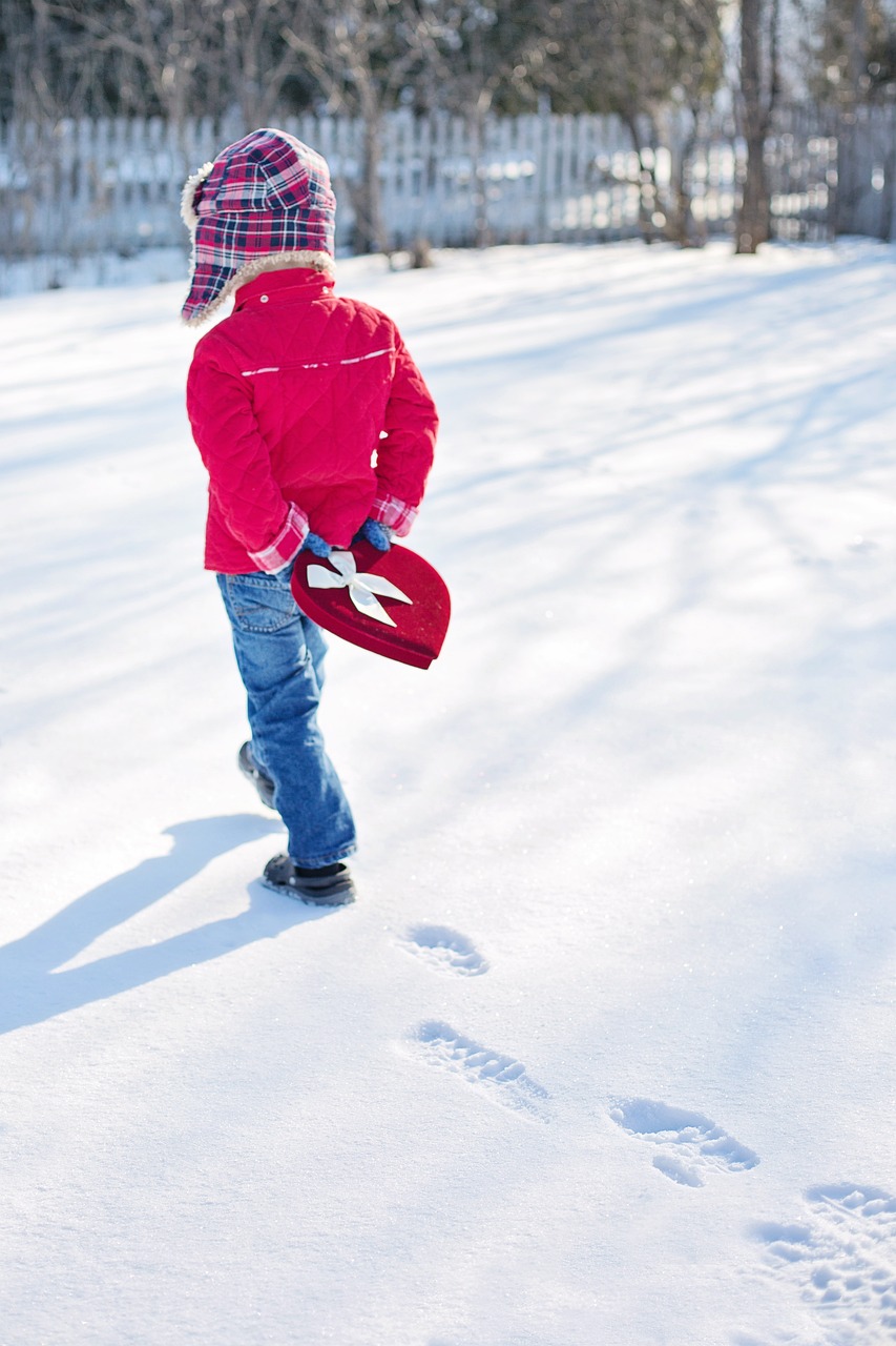 Child with a heart box of candy behind their back, in snow