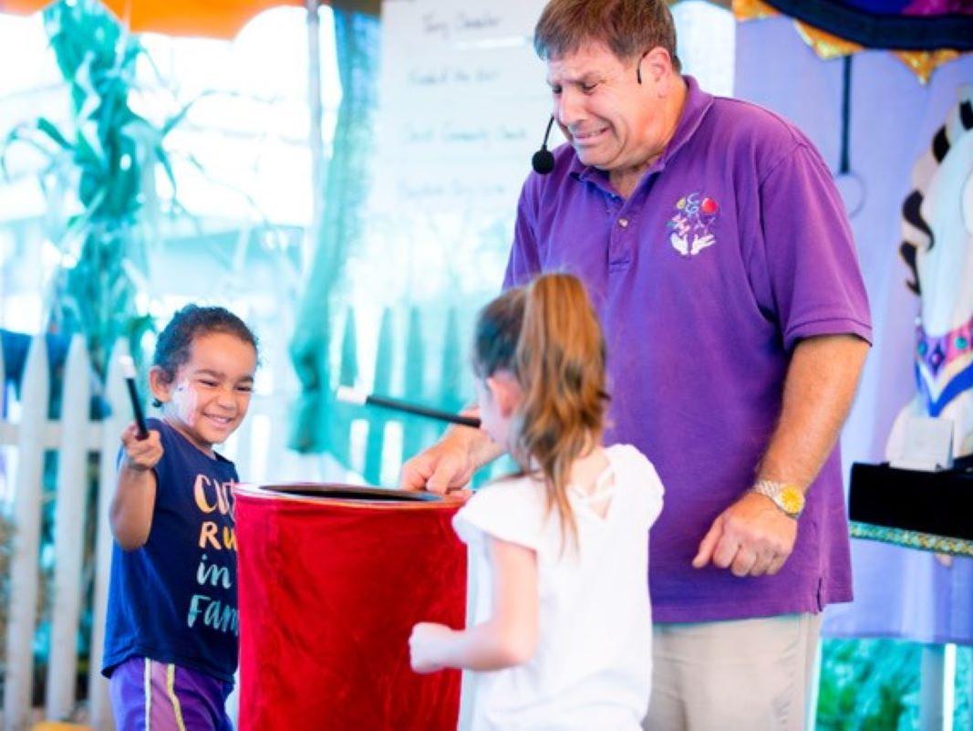 Magician with two children with magic wands surrounding a red bag. 