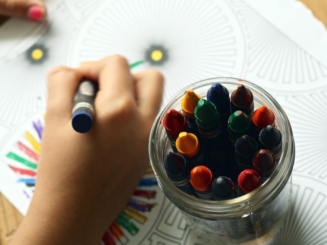 Kid's hand holding crayons and coloring.