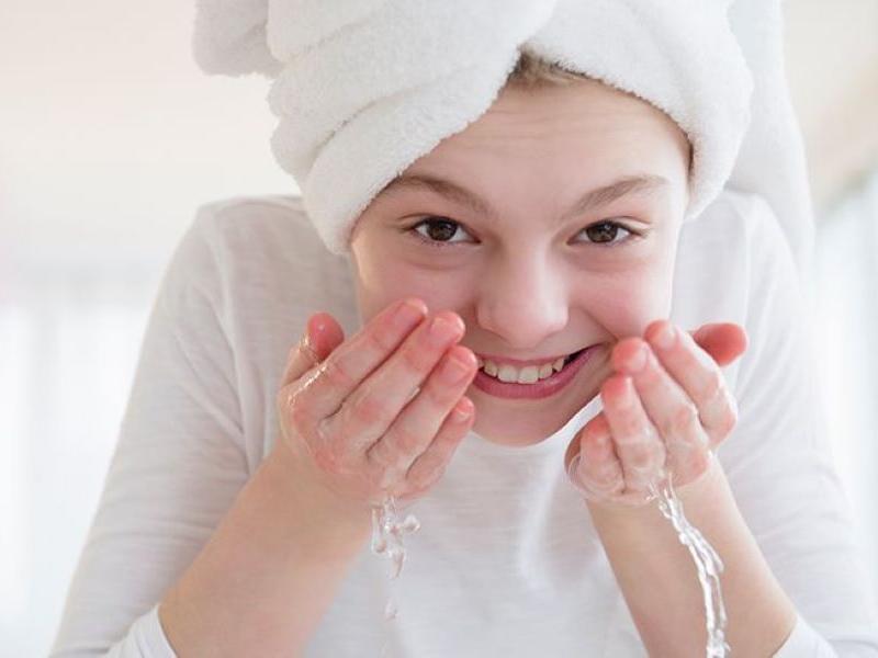 Young girl with her hair in a towel washing her face.