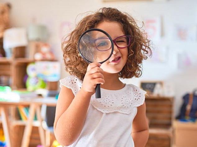 Little girl with glasses looking through a magnifying glass.